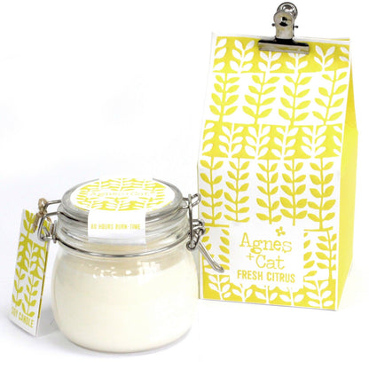 A traditional clear glass Kilner jar filled with a white scented candle and adorned with a yellow patterned decorative tag.