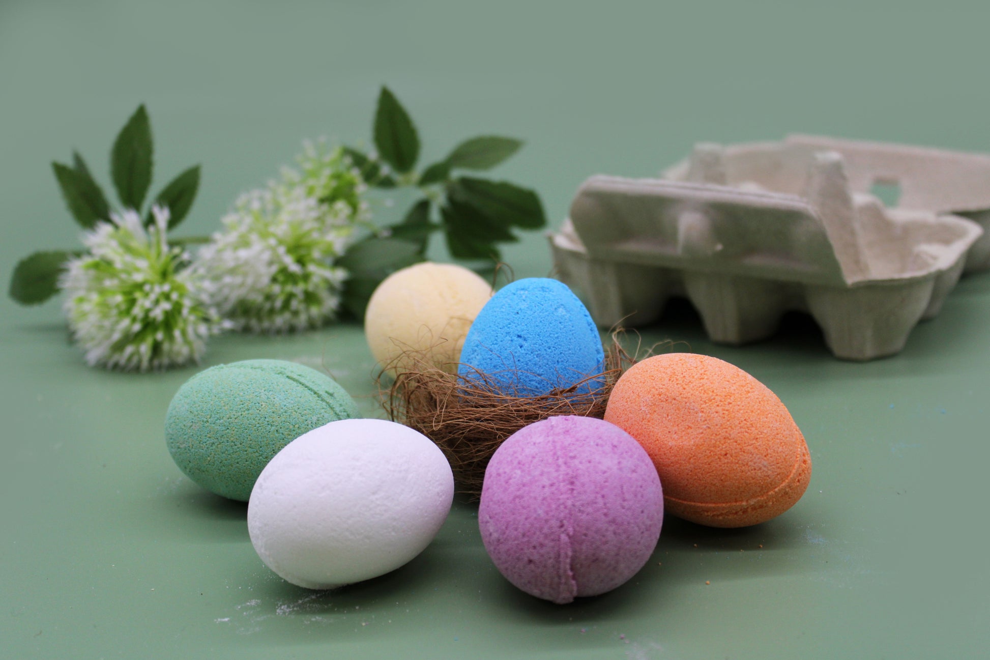 A cardboard egg carton filled with six different colored egg-shaped bath bombs, perfect for a Spring or Easter gift set.