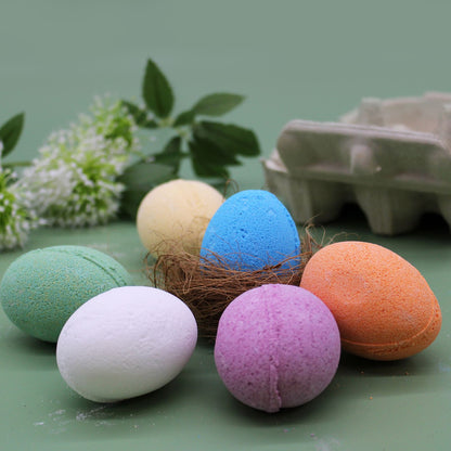A cardboard egg carton filled with six different colored egg-shaped bath bombs, perfect for a Spring or Easter gift set.