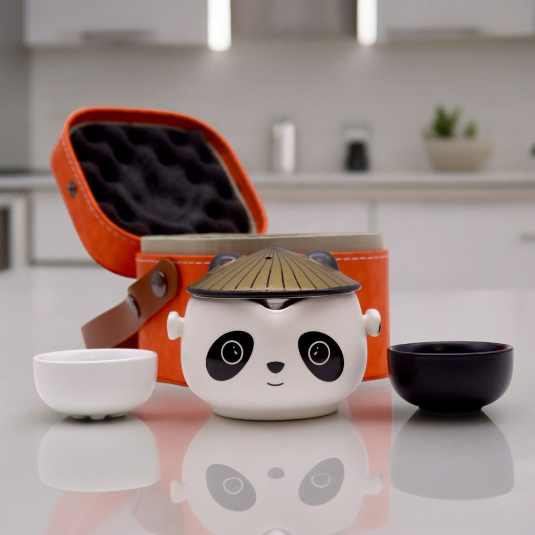 A vibrant orange travel case containing a compact black ceramic teapot and two stacking cups featuring panda illustrations.