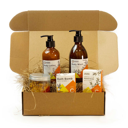A luxury gift set containing Vitamin C bath salts, body lotion, and face serum arranged with decorative dried orange slices.