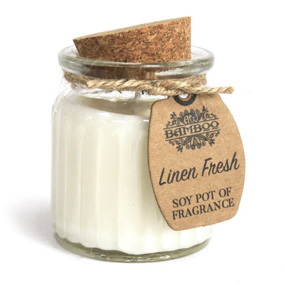 A cream-colored soy wax candle in a small glass pot with a cork lid, featuring a clean linen fresh scent.