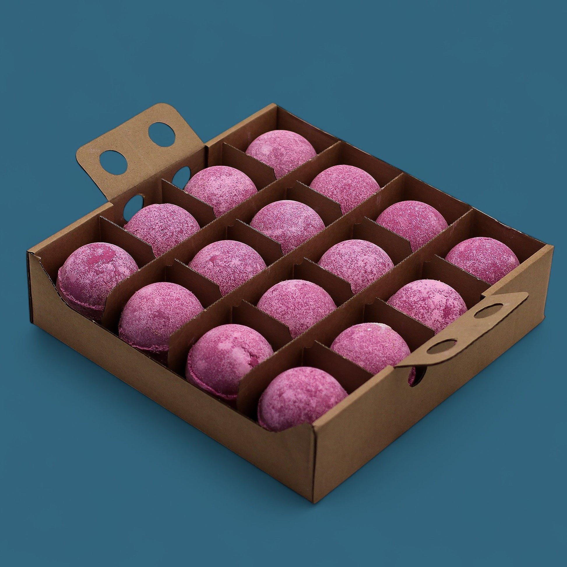 A wooden display box holding sixteen large, deep pink cherry-scented bath bombs arranged in a bulk grid.