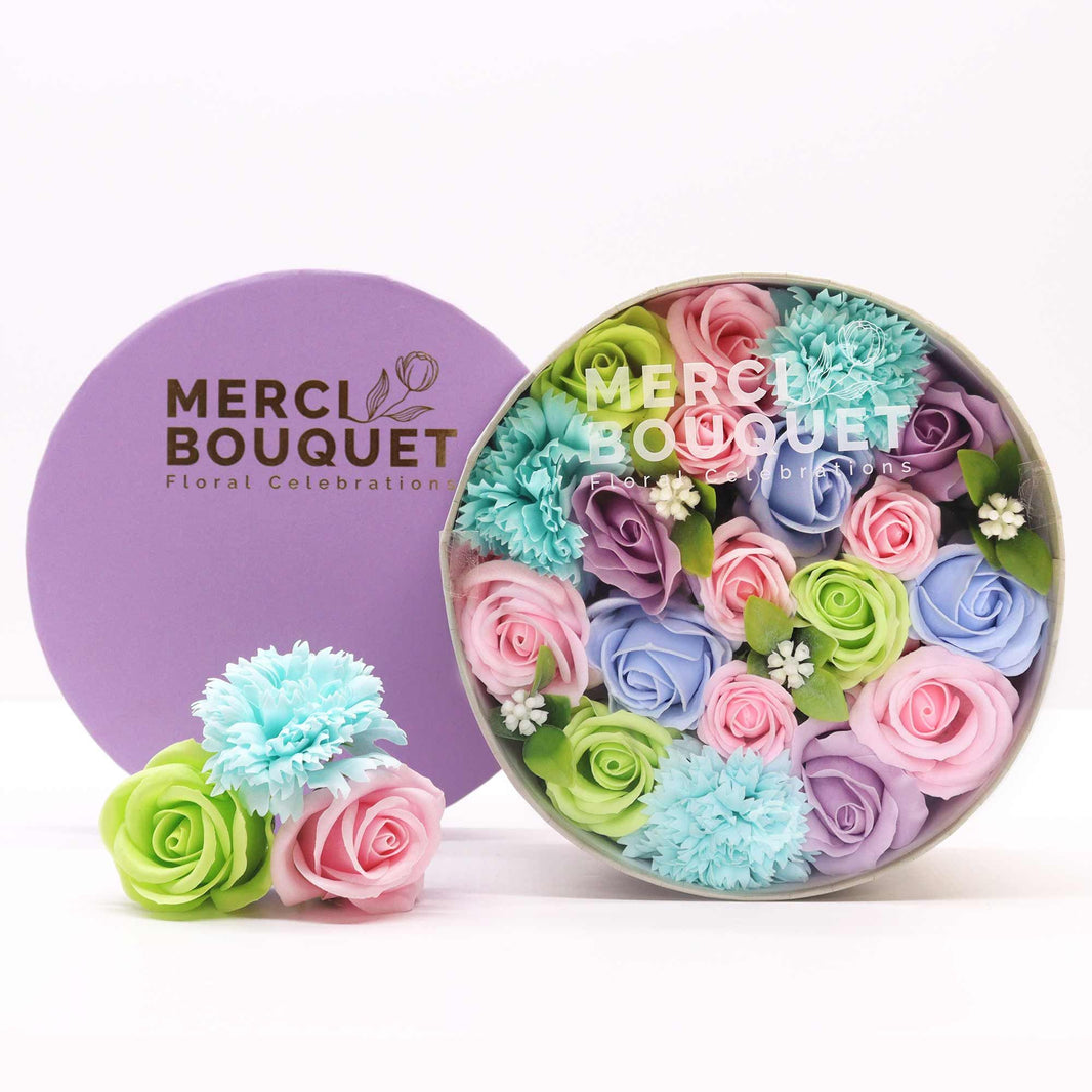 A round decorative gift box containing a soft arrangement of blue and white soap flowers for baby showers.