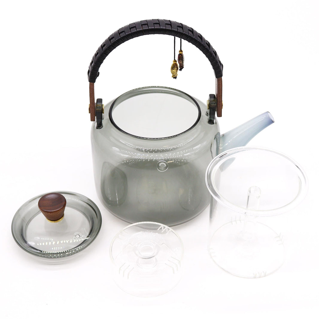 A large, clear borosilicate glass teapot with a charcoal-toned lid and handle, featuring a unique internal steamer infuser.