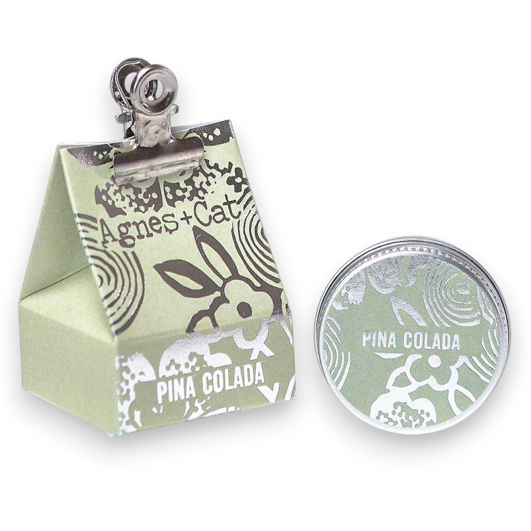 A 20g tin of Pinacolada flavored organic lip balm featuring a tropical pineapple and coconut design on the packaging.