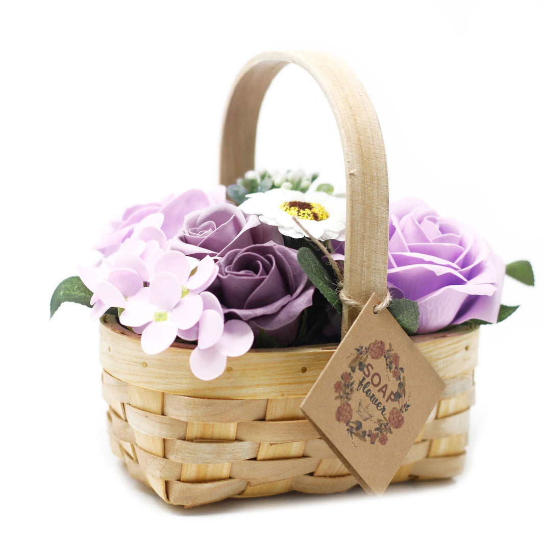A decorative wicker basket arrangement of realistic purple and lilac soap flowers with lush greenery.