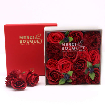 A red square gift box packed with realistic, deep red soap rose flowers.