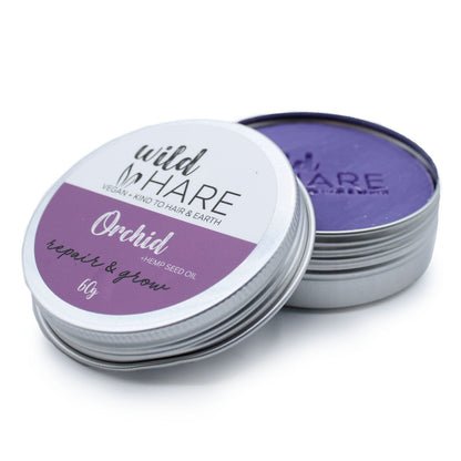 A 60g Wild Hare solid shampoo bar with a purple floral orchid label, stored in a reusable metal travel tin.