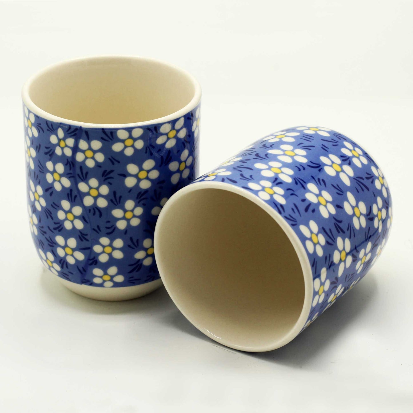 Two white ceramic tea cups with a dark blue background and white daisy patterns, perfect for herbal tea rituals.