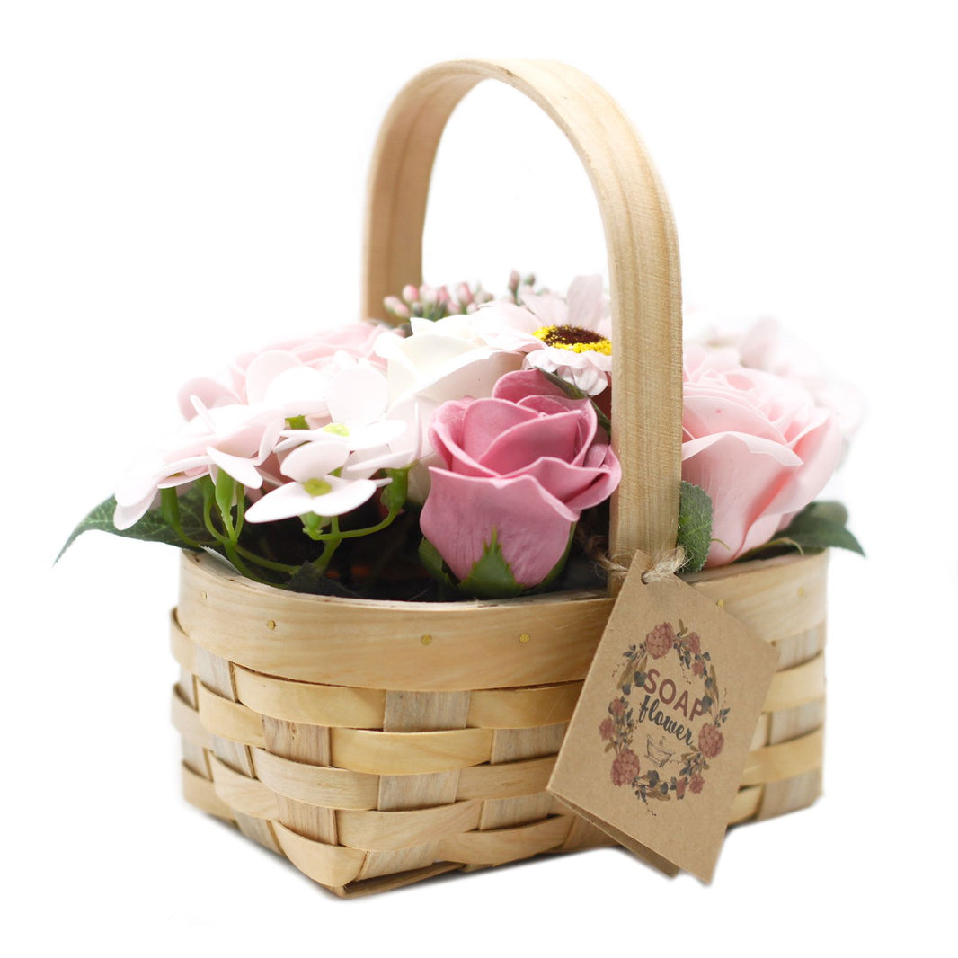 A medium-sized wicker gift basket featuring an arrangement of realistic pink soap roses and white flowers with greenery.