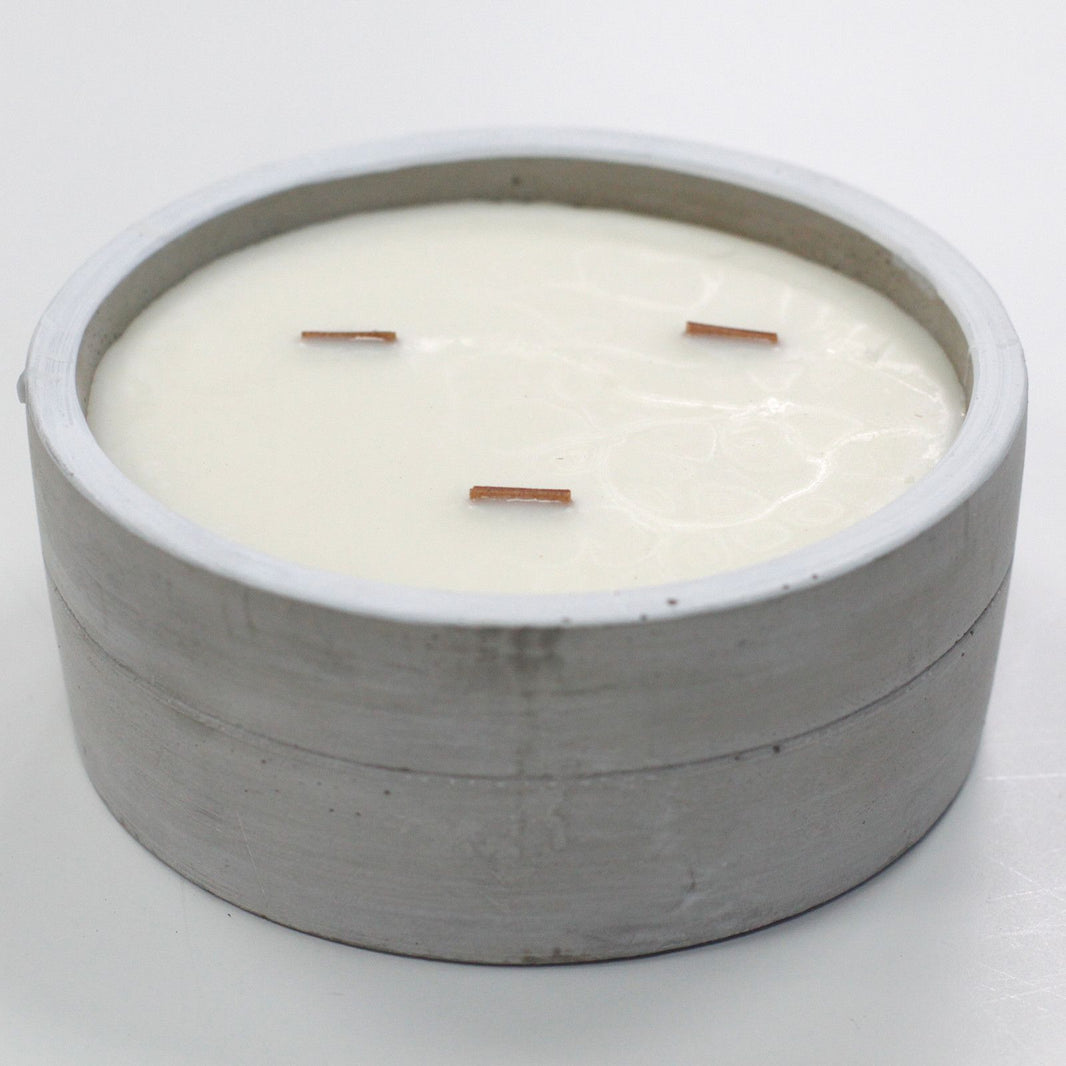 A large, round grey concrete candle bowl containing three wicks set in white soy wax.