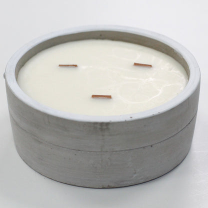 A large, round grey concrete candle bowl containing three wicks set in white soy wax.