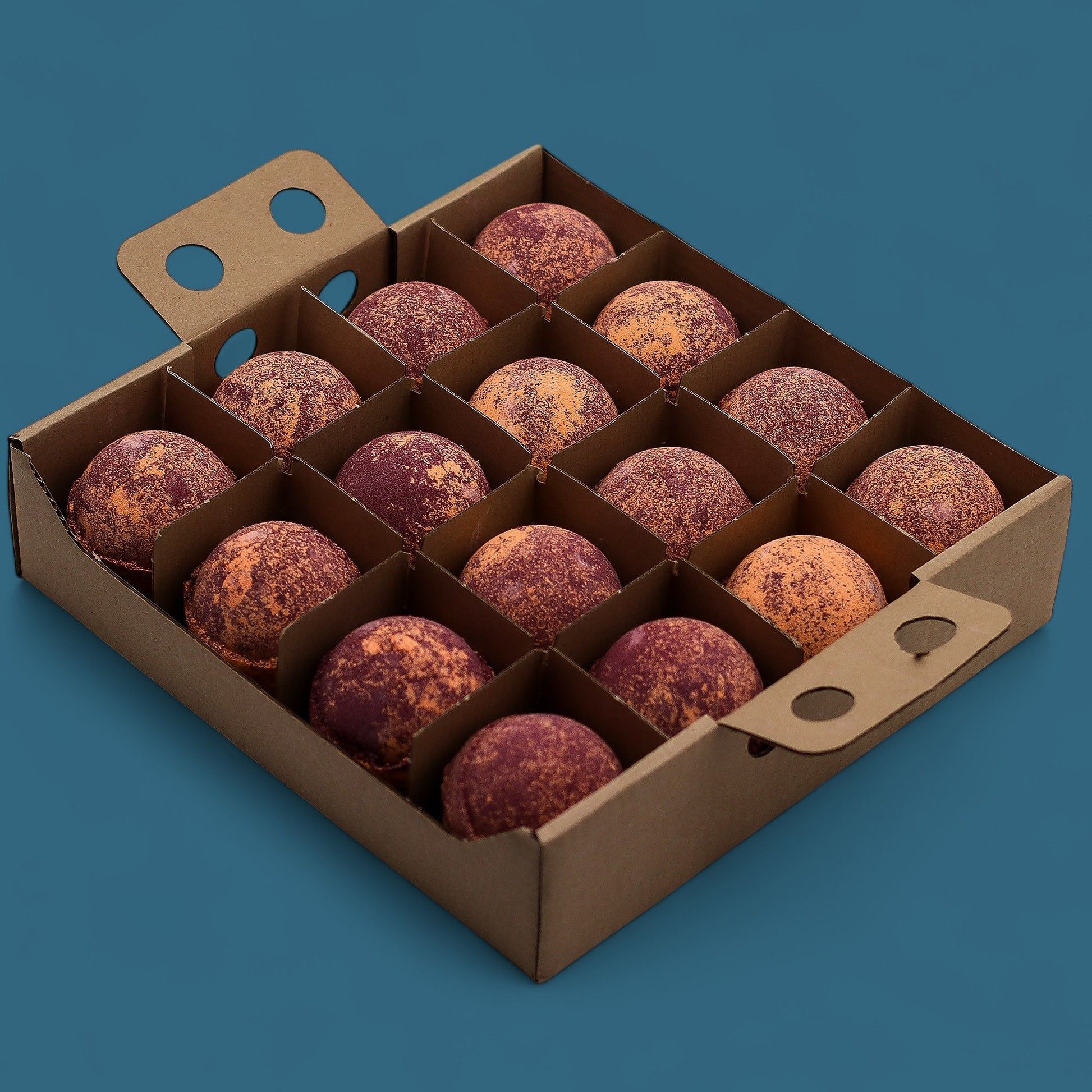 A dark wooden tray holding sixteen jumbo chocolate and orange marbled bath bombs arranged in a neat grid for professional display.
