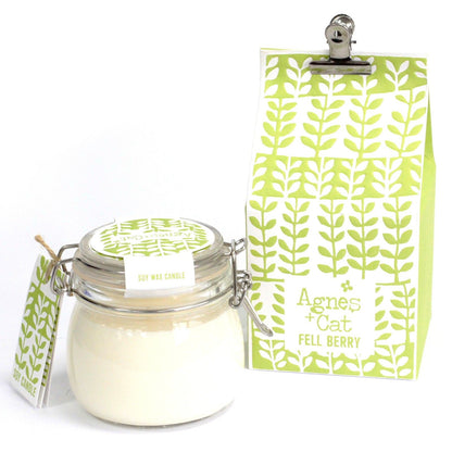 A clear glass preserve-style jar with a metal clip-top lid, housing a white scented candle with a green floral hanging tag.