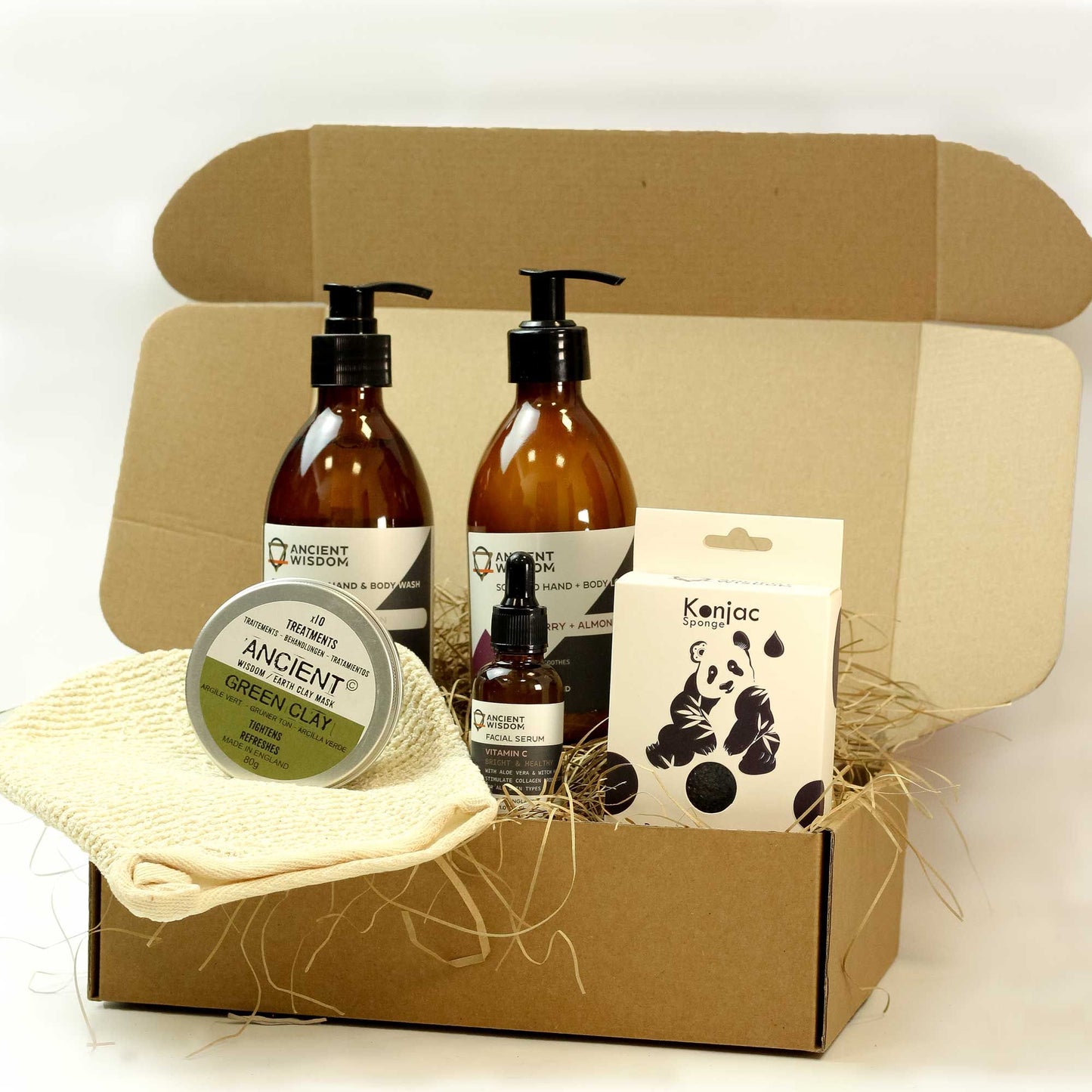 A premium kraft gift box containing amber glass bottles of facial wash, a soft cloth, and a small botanical soap bar on natural wood wool.