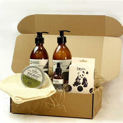 A premium kraft gift box containing amber glass bottles of facial wash, a soft cloth, and a small botanical soap bar on natural wood wool.