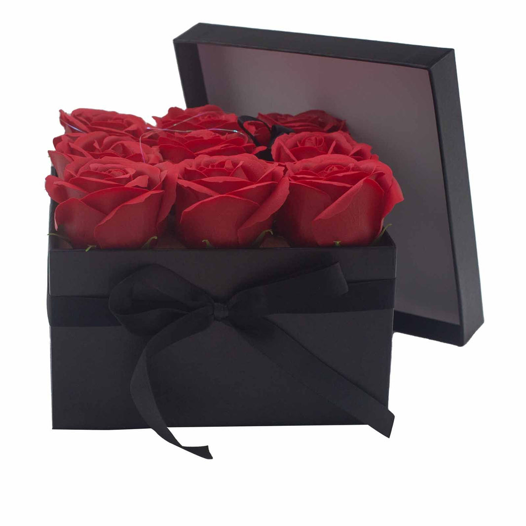 A black square gift box featuring 9 realistic red soap roses arranged in a classic floral display.