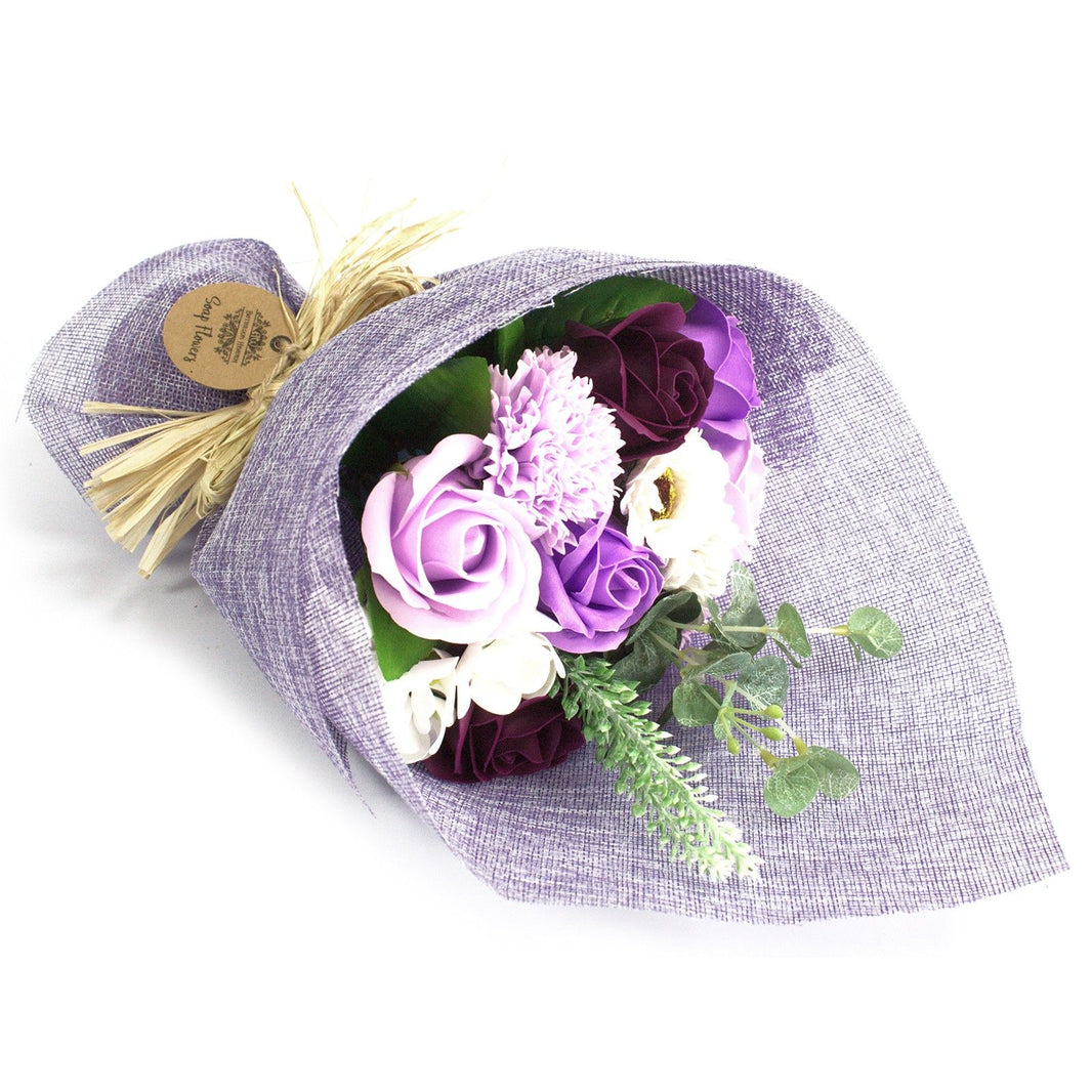 A standing bouquet of realistic purple and lavender soap flowers wrapped in decorative paper with a purple ribbon.
