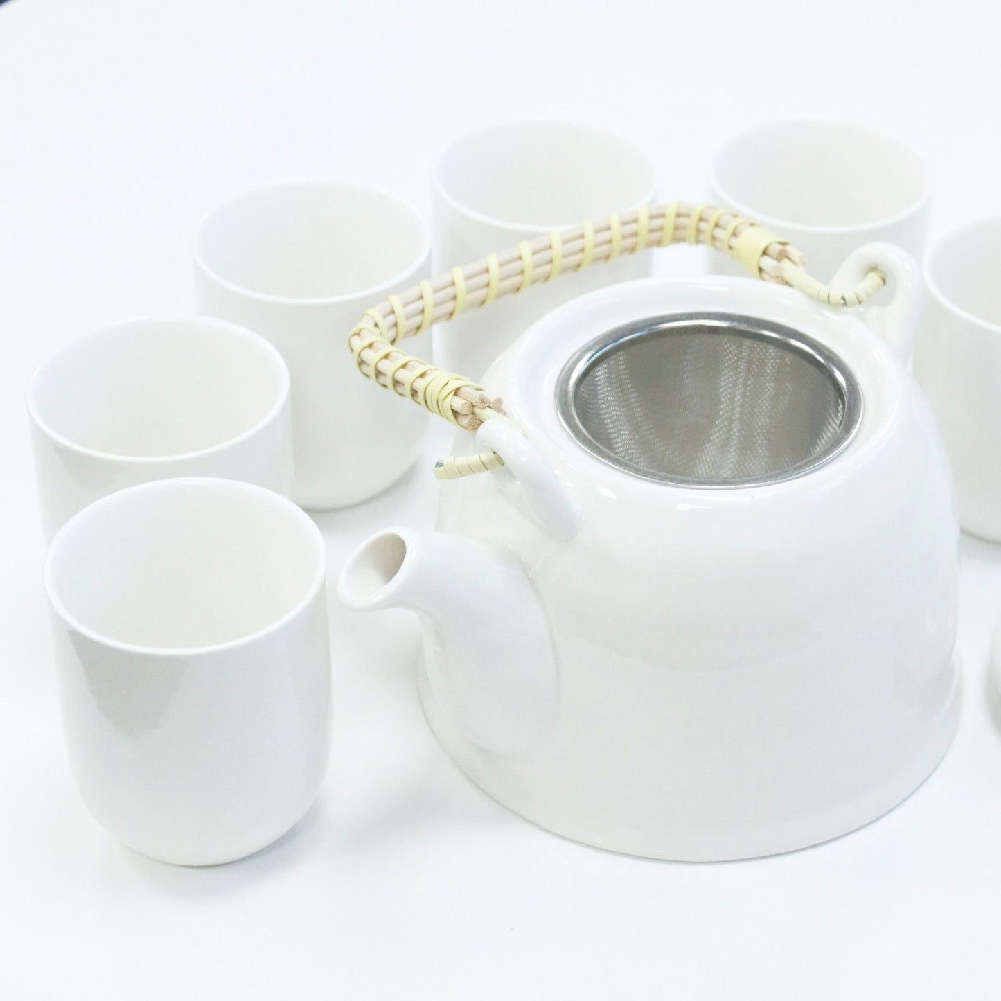 A clean, bright white ceramic teapot set including a teapot with a bamboo handle and matching white handleless cups.