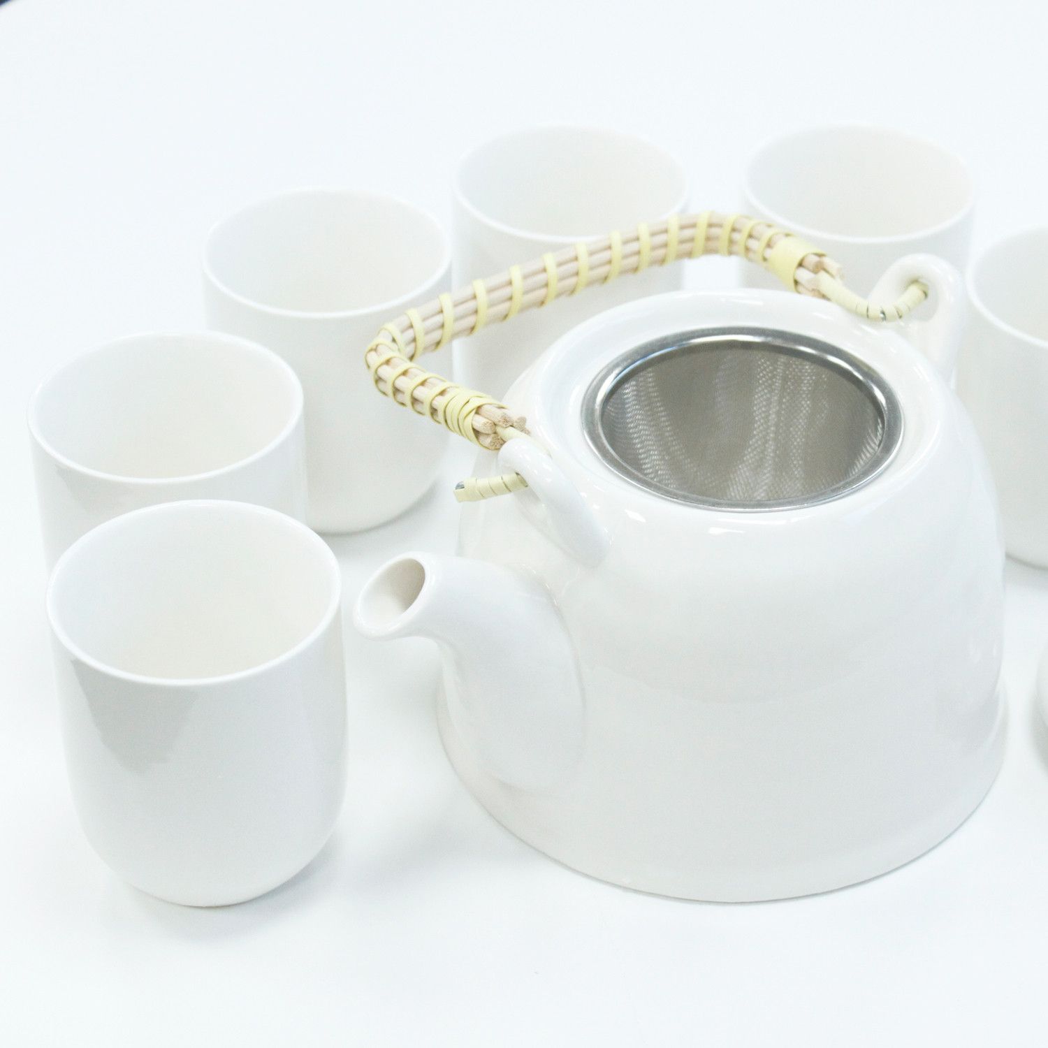 A clean, bright white ceramic teapot set including a teapot with a bamboo handle and matching white handleless cups.