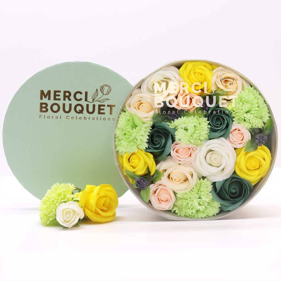 A decorative round gift box filled with realistic yellow and green soap flowers designed to look like a fresh Spring bouquet.