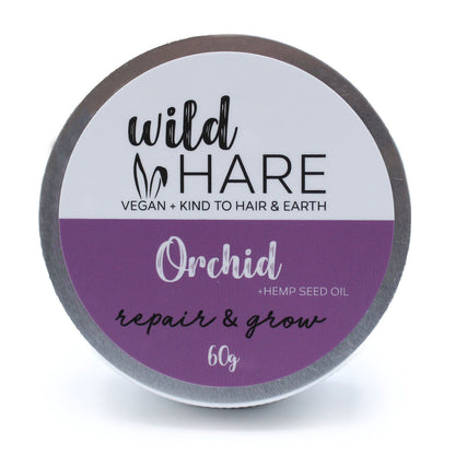 A 60g Wild Hare solid shampoo bar with a purple floral orchid label, stored in a reusable metal travel tin.