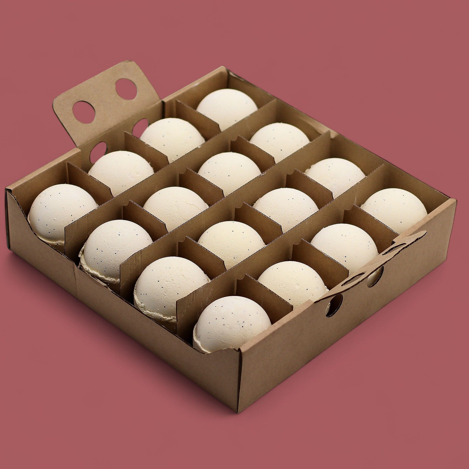 A cardboard display box holding 16 individually wrapped 180g vanilla bath bombs in cream tones.
