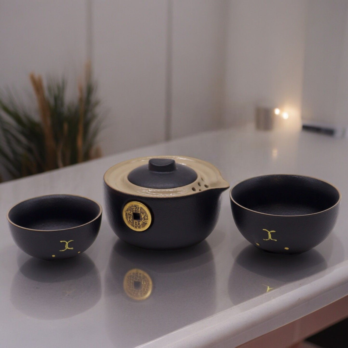 A matte black ceramic travel tea set featuring a gold Maneki-neko lucky cat design on the teapot and two matching small cups.