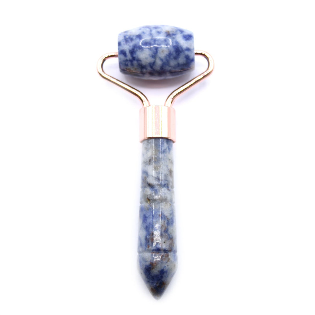 A handheld beauty tool with a polished blue and white marbled Sodalite gemstone roller on a rose gold handle.