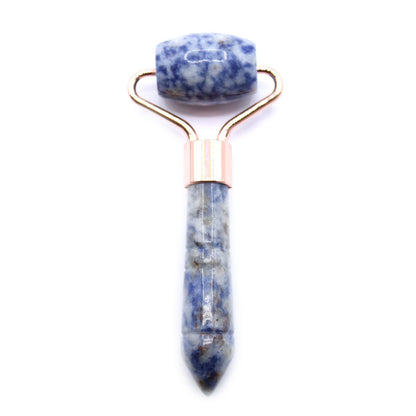 A handheld beauty tool with a polished blue and white marbled Sodalite gemstone roller on a rose gold handle.
