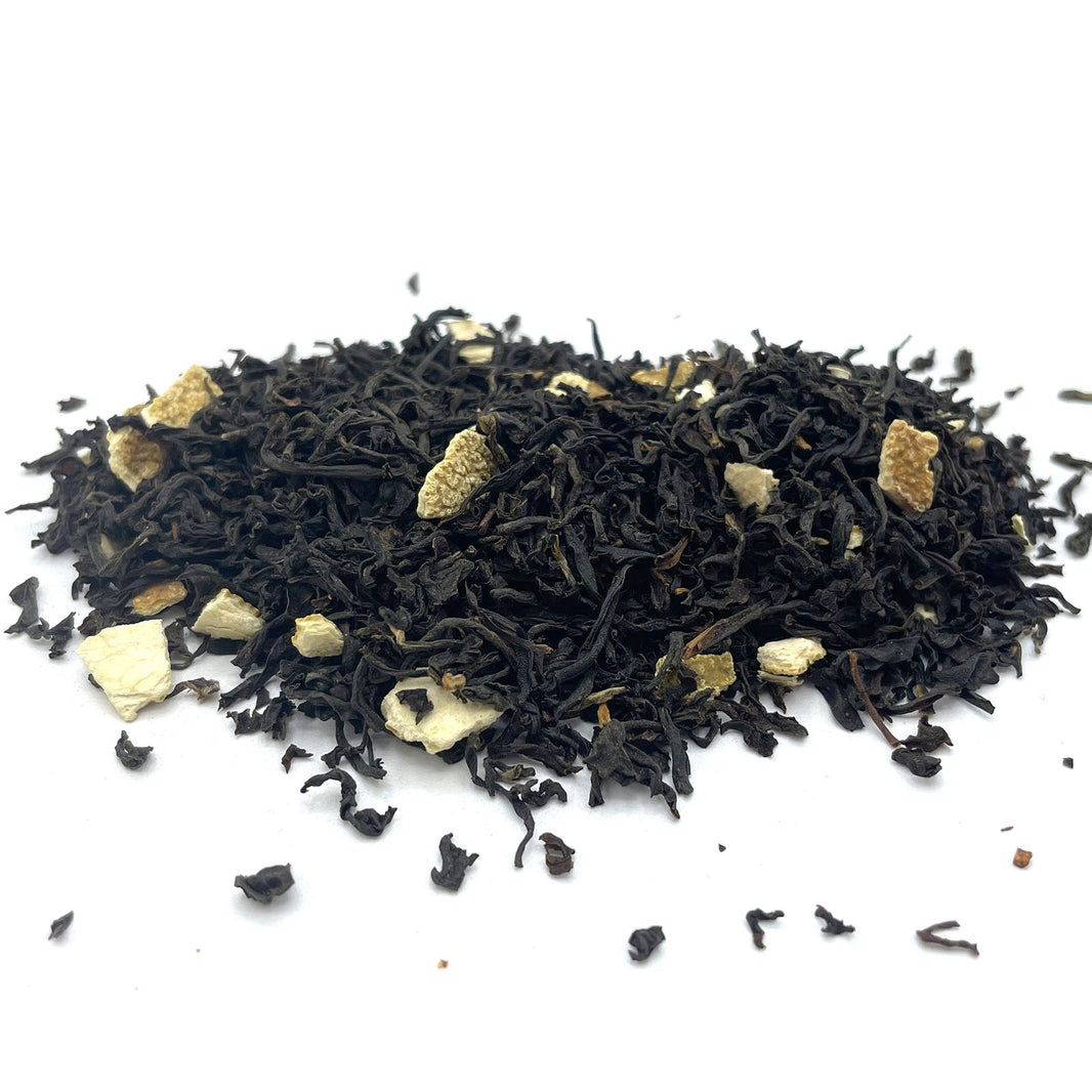 Bulk black loose-leaf tea leaves mixed with bright, dehydrated orange peel pieces and colorful flower petals.