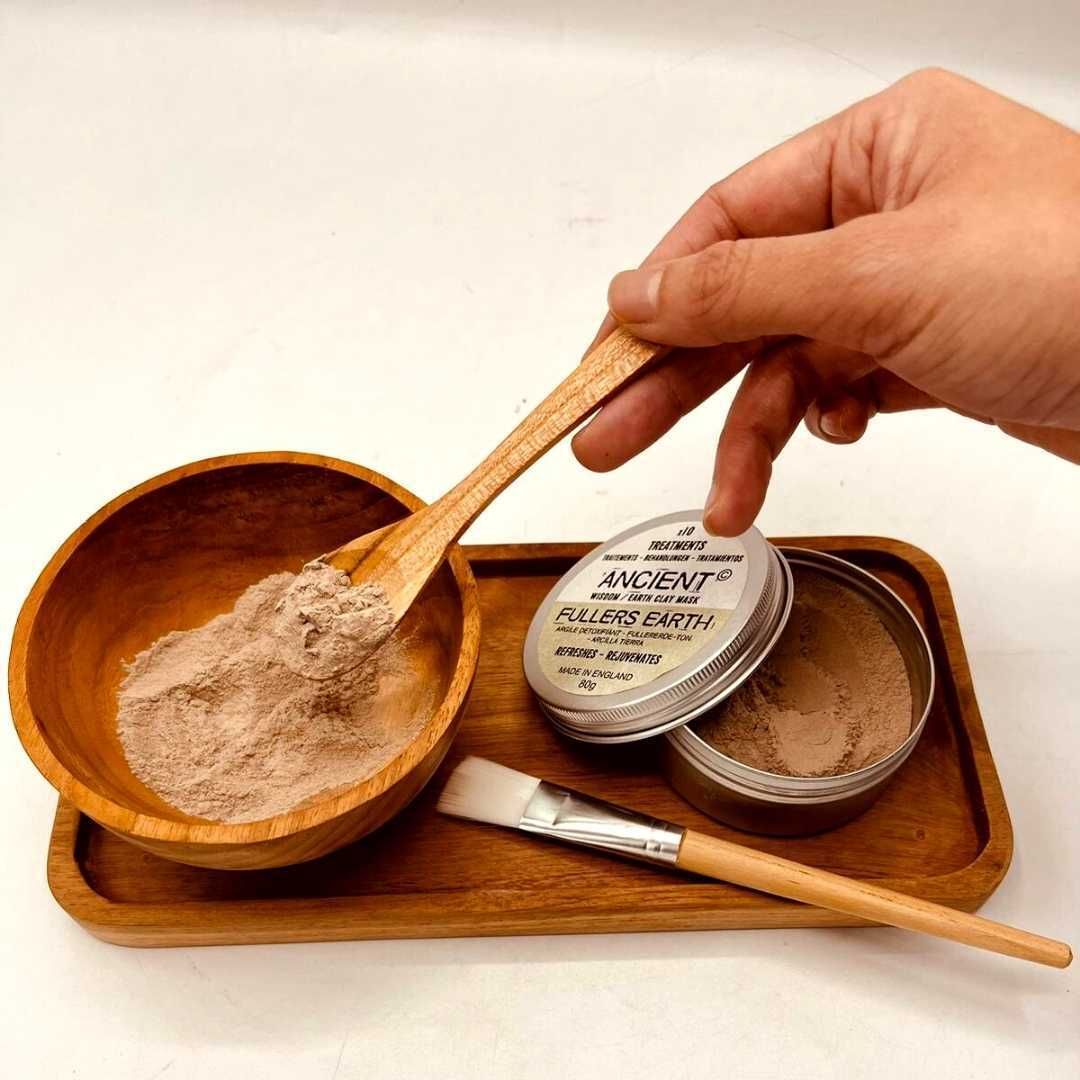A wooden spa application kit featuring a natural bowl, a soft application brush, and a wooden spatula on a matching tray.