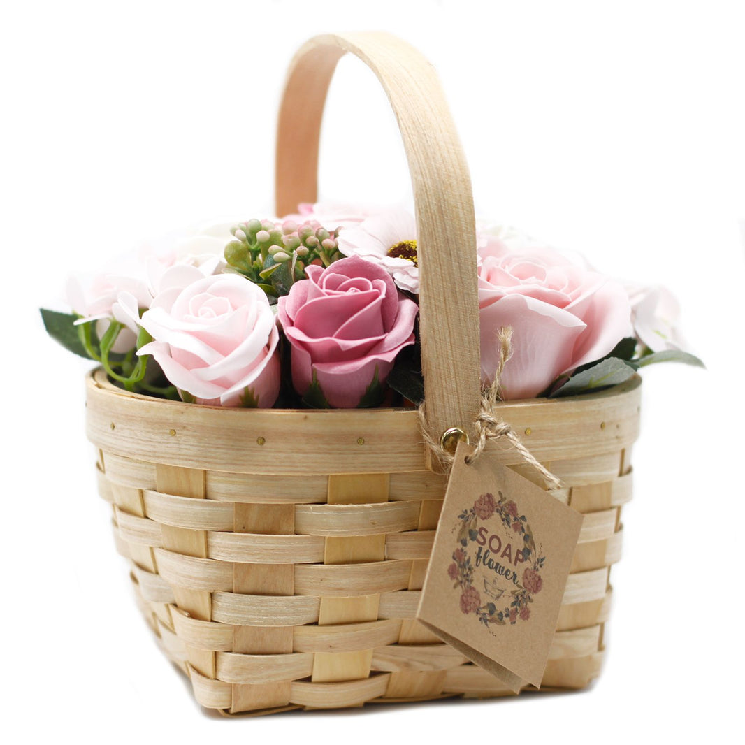 A large decorative wicker basket overflowing with realistic pink and cream soap roses and lush greenery.