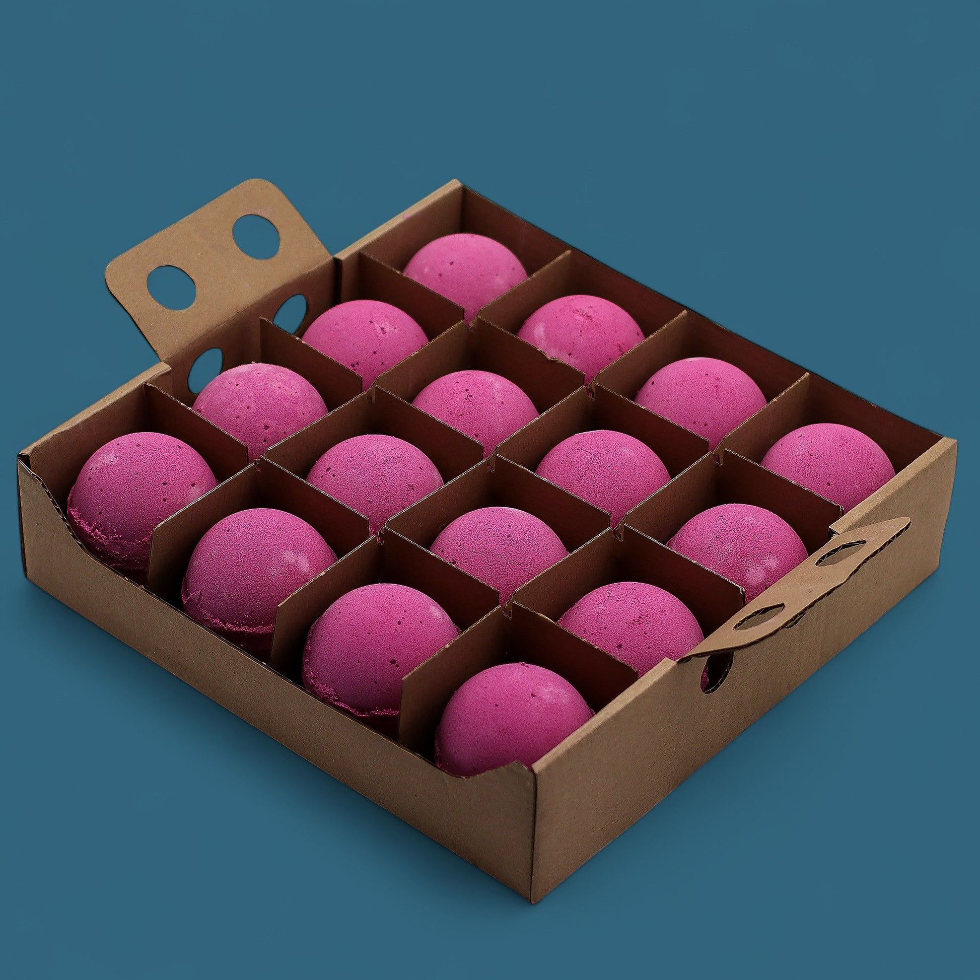 A wooden display tray holding a bulk grid of sixteen large, vibrant pinkish-red cranberry scented bath bombs.