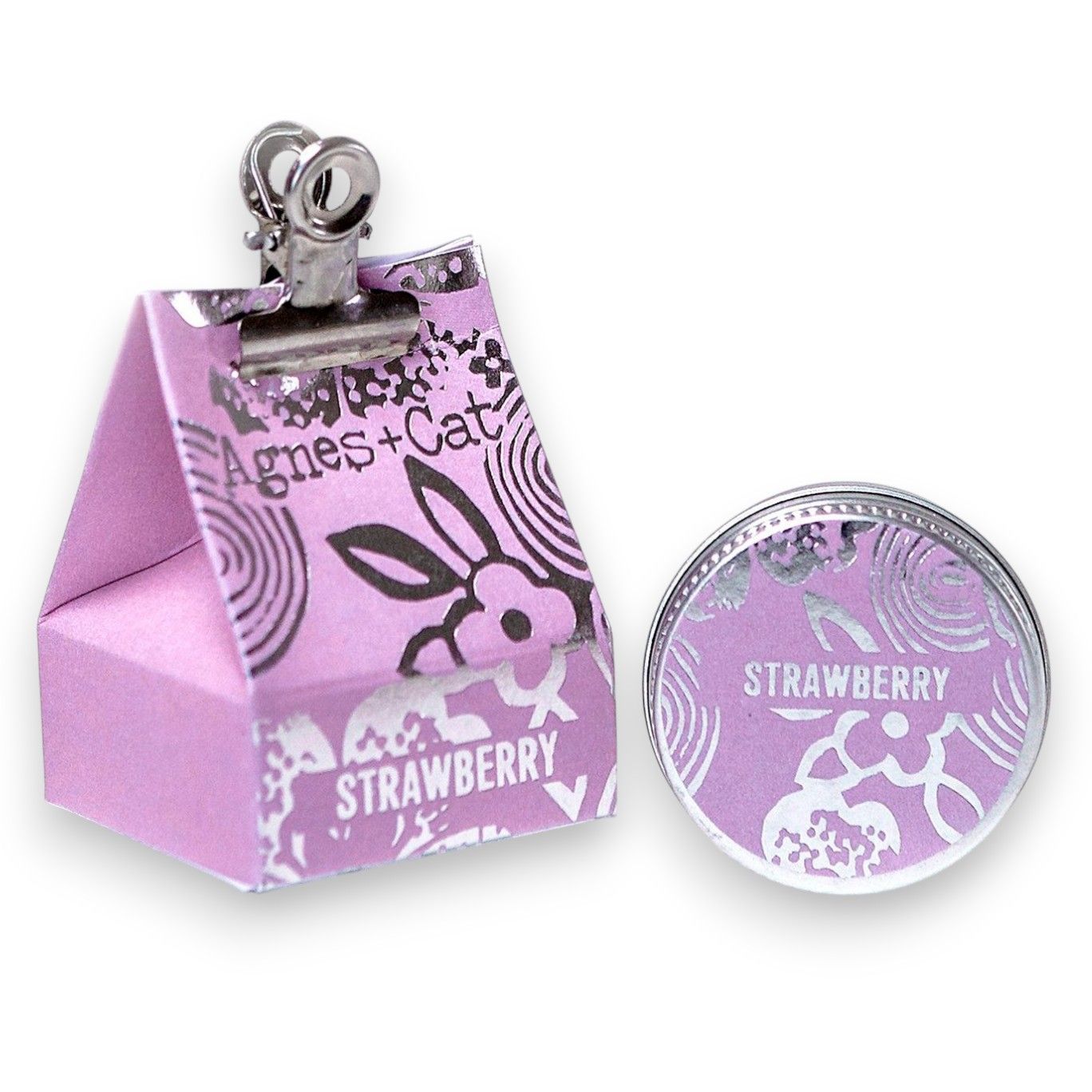 A 20g round tin of strawberry-scented lip balm shown with its pink and purple floral gift packaging.