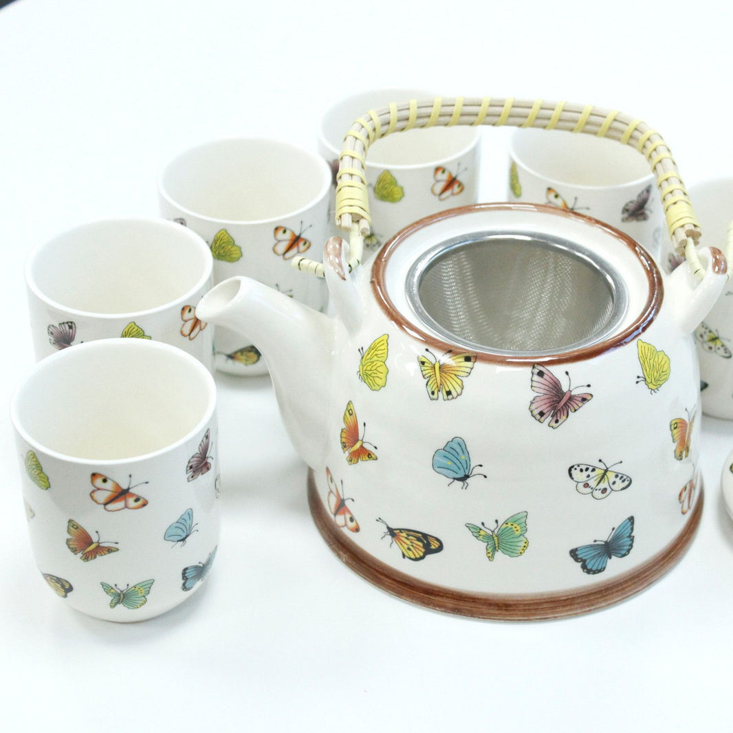 A white ceramic herbal teapot set with vibrant butterfly and floral patterns, including a teapot and small cups.