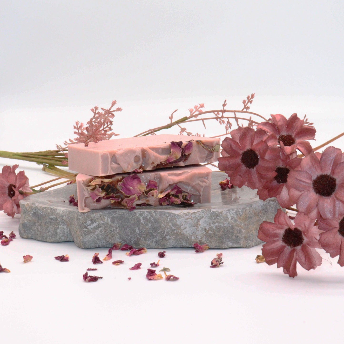 A luxury artisan soap slice with rose-pink and cream swirls topped with real dried rosebuds and petals.