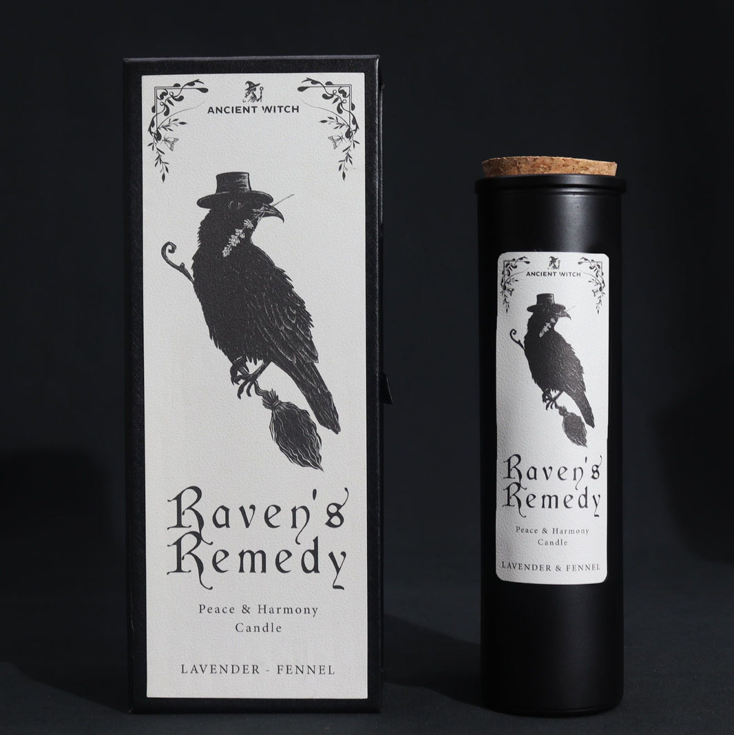 A sleek black pillar candle in a decorative black cardboard sleeve featuring a raven and occult symbols.