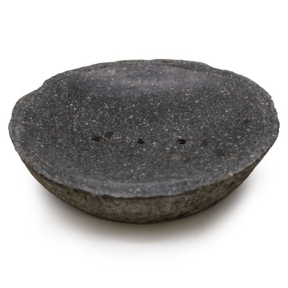 A dark, hand-carved natural riverstone soap dish with a smooth hollow and organic exterior shape.