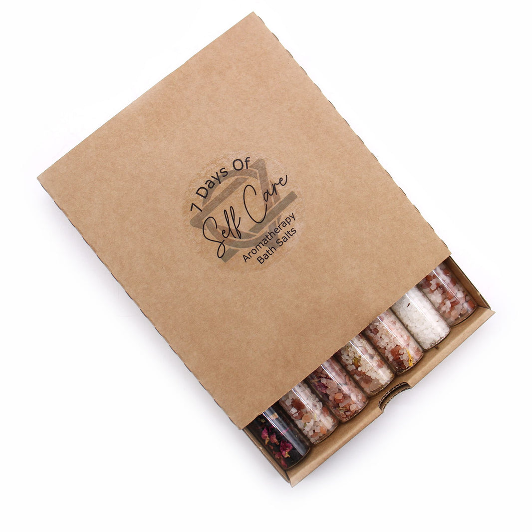 A rustic kraft paper gift box showcasing seven glass vials filled with colorful, layered aromatic bath salts.