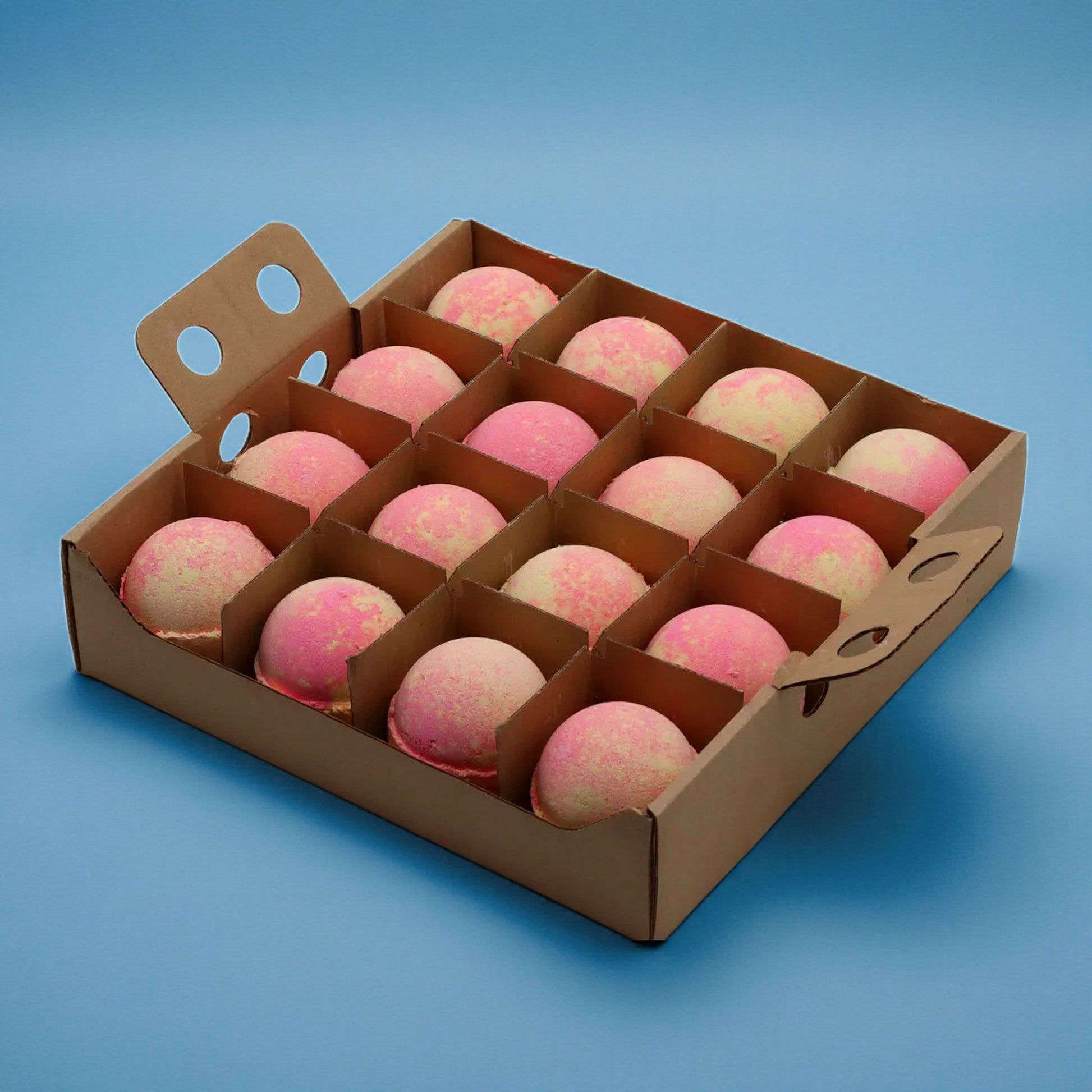 A bulk wooden display box containing sixteen round, pink-marbled bath bombs arranged in a neat grid.