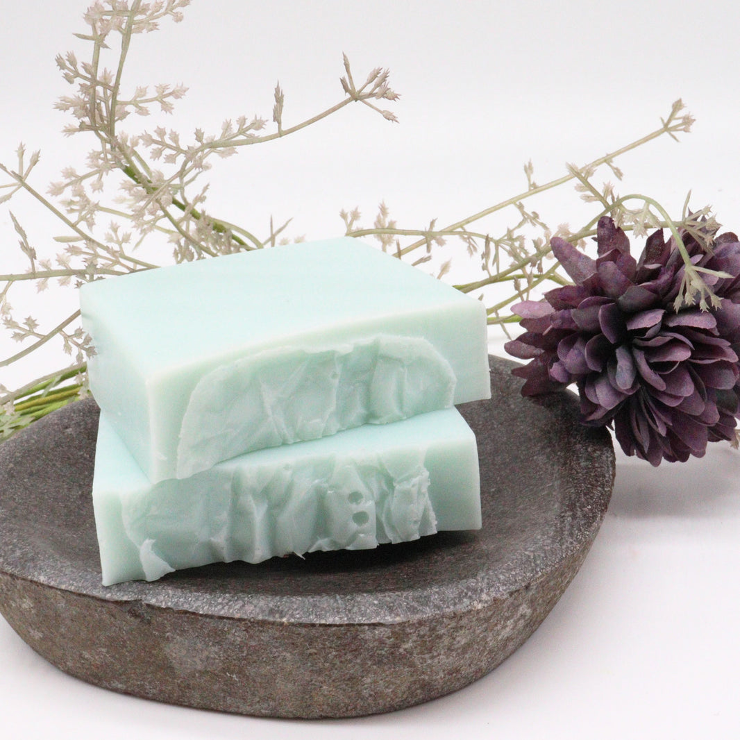 A handcrafted soap slice featuring a marbled blue and white design with dried botanical tea leaves on a rustic stone surface.