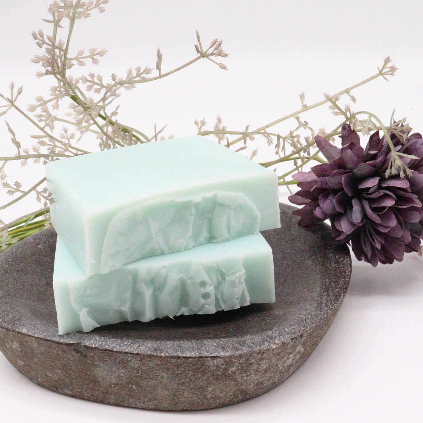 A handcrafted soap slice featuring a marbled blue and white design with dried botanical tea leaves on a rustic stone surface.