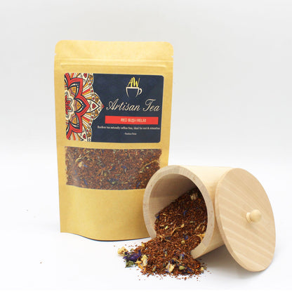 A cylindrical cardboard tea container with a yellow and brown "Red Bush Relax" label and loose tea leaves nearby.