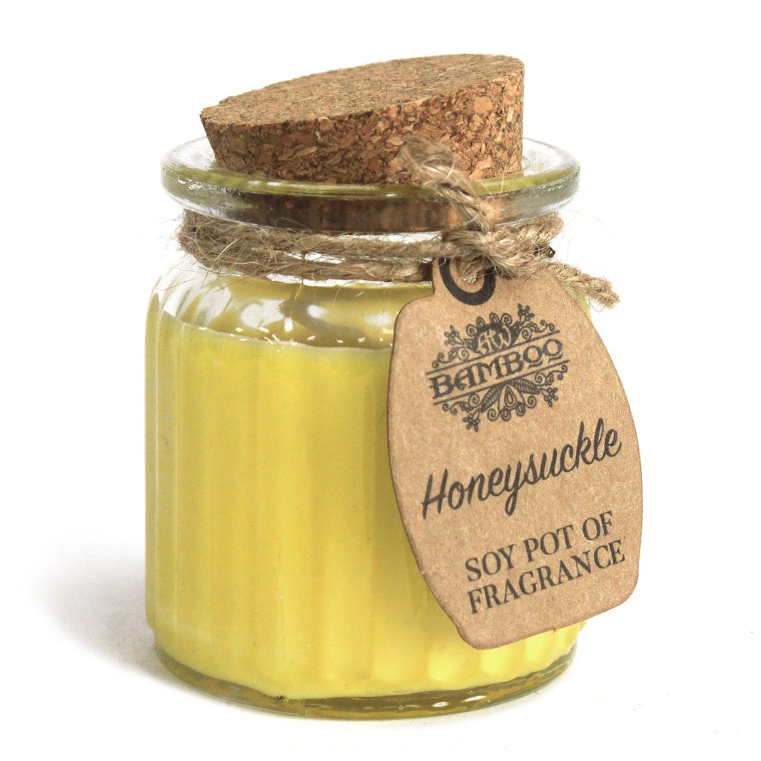 A small glass jar candle with yellow-tinted wax, a cork stopper, and a tag illustrated with honeysuckle vines.