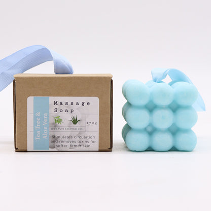 A blue massage soap bar with textured nubs for muscle relief, scented with tea tree and aloe vera, in its individual box.