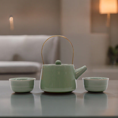 A sleek, modern jade-green ceramic teapot with a clean cylindrical shape and two matching handleless tasting cups.