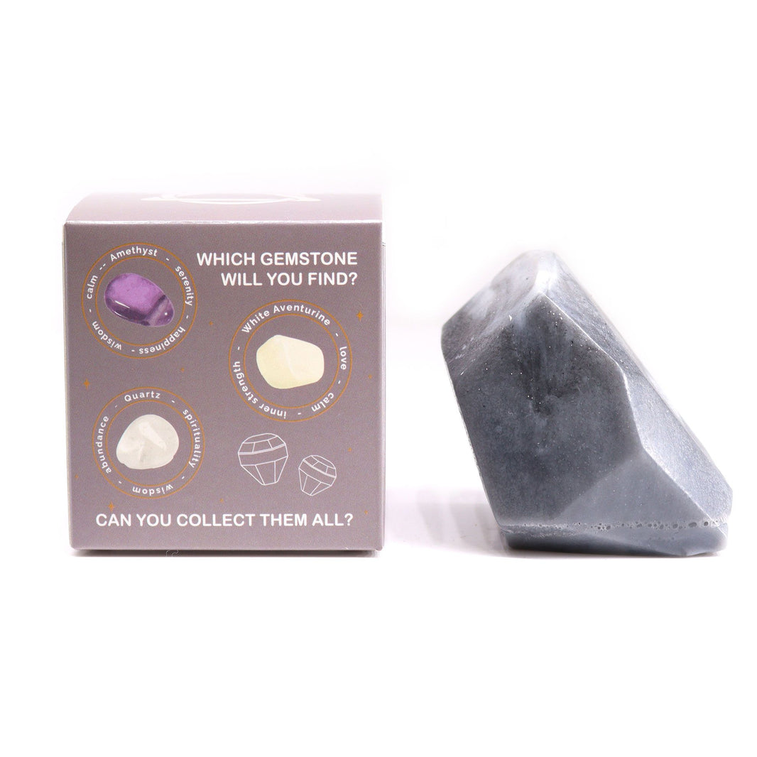 A translucent, charcoal-grey artisan soap bar shaped like a rough-cut crystal gemstone cluster in a themed gift box.