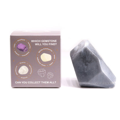 A translucent, charcoal-grey artisan soap bar shaped like a rough-cut crystal gemstone cluster in a themed gift box.